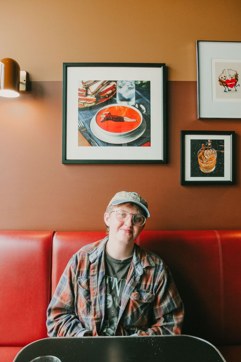 Restaurant interior with framed food artwork on terracotta walls and red booth seating.