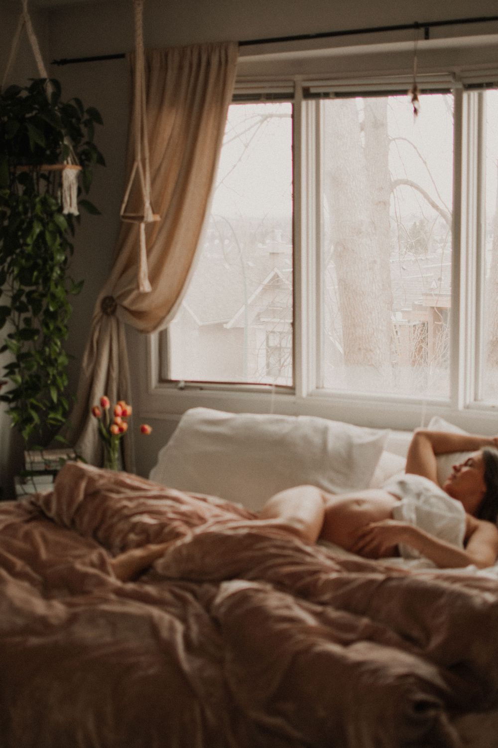 Cozy bedroom with sunlit window, flowing curtains, and rumpled bedding.