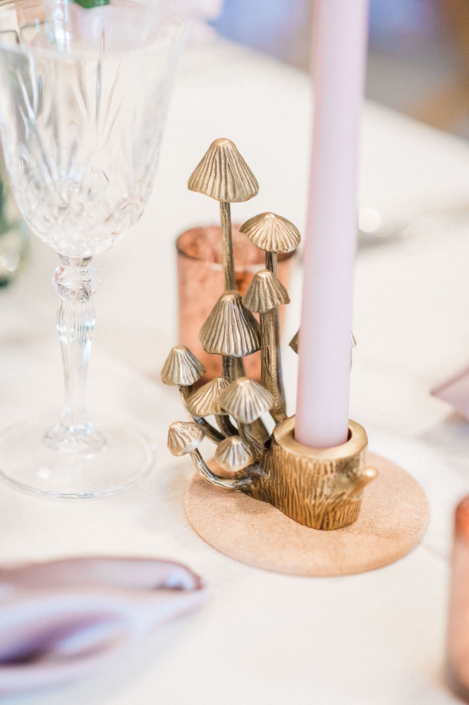 Gold mushroom-shaped candle holders with white tapered candles create an elegant table setting with crystal glassware.