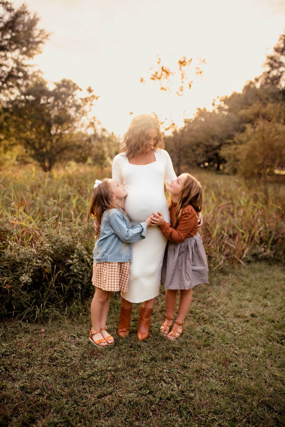 Tender moment between children and woman in white dress during golden hour.