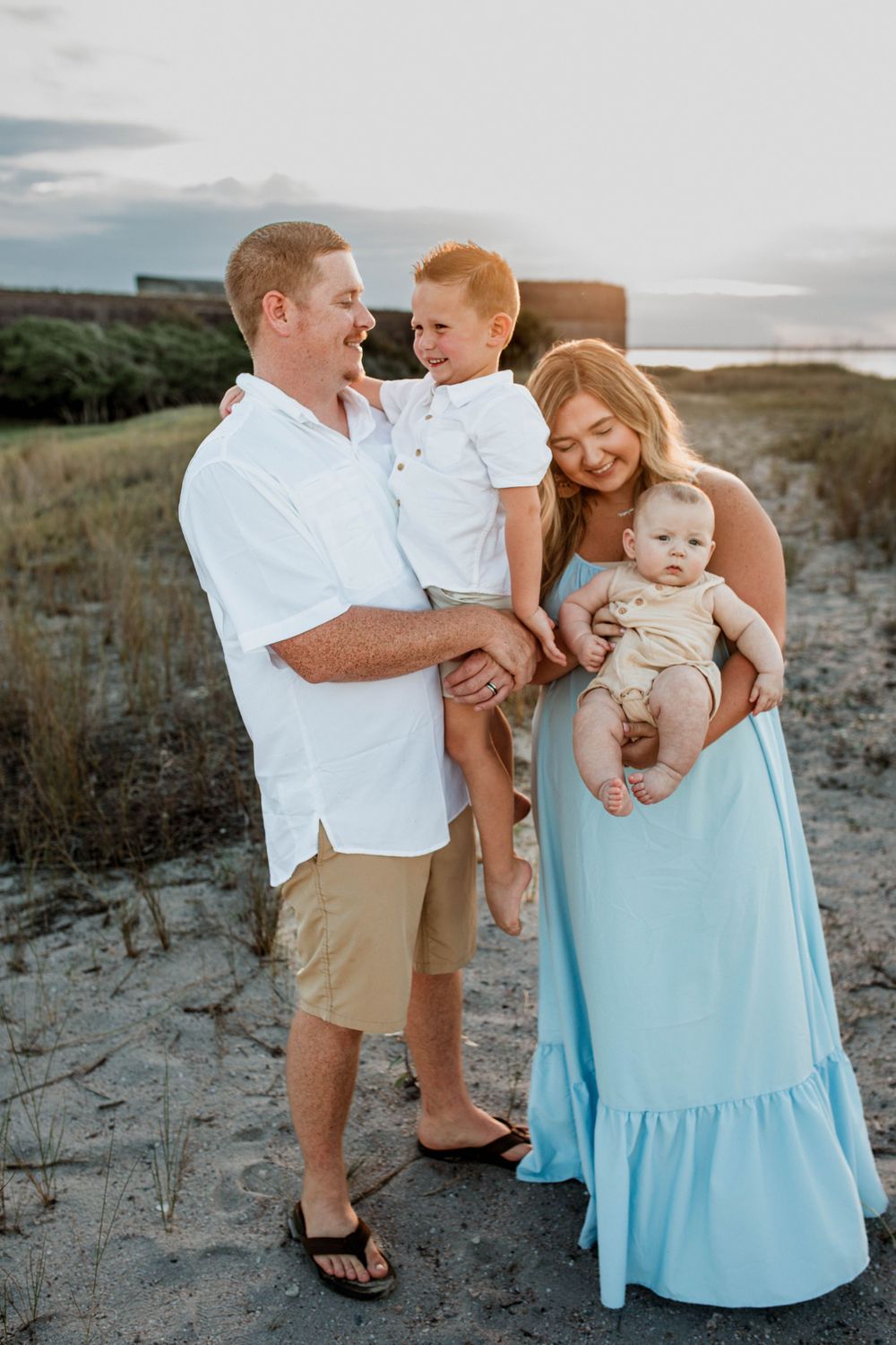 Family portrait on beach at sunset with parents holding two small children.