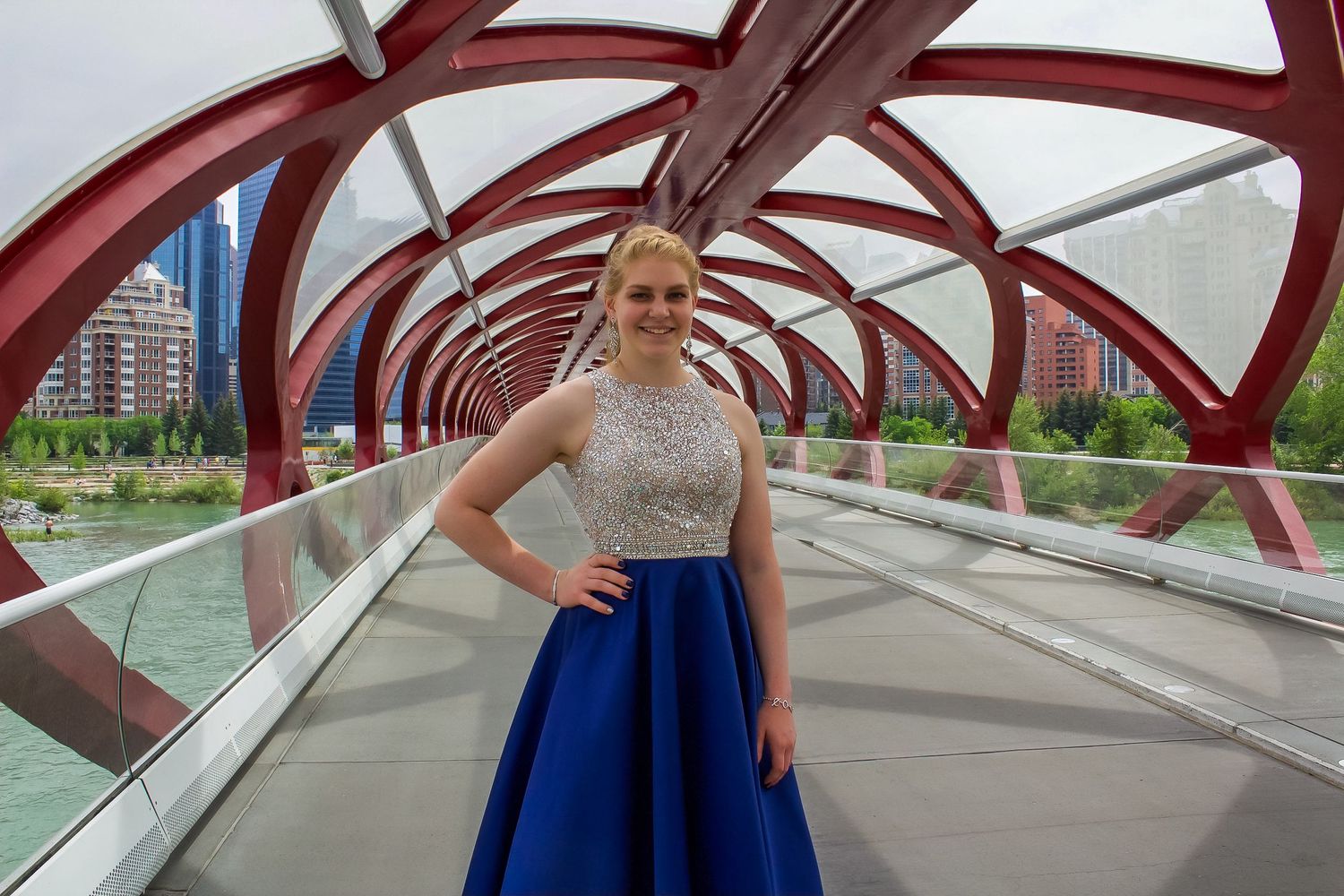 a young women in a blue and silver dress stands confidently on a bridge.