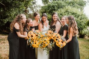 Wedding party holding sunflower bouquets outdoors in summer garden setting.