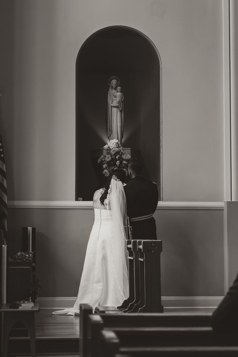 Black and white photo of empty church interior with wedding dress displayed.
