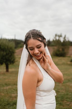 Bride in elegant white dress laughs joyfully during outdoor wedding photoshoot.