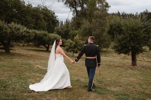 Newlyweds walk hand in hand through scenic outdoor field.