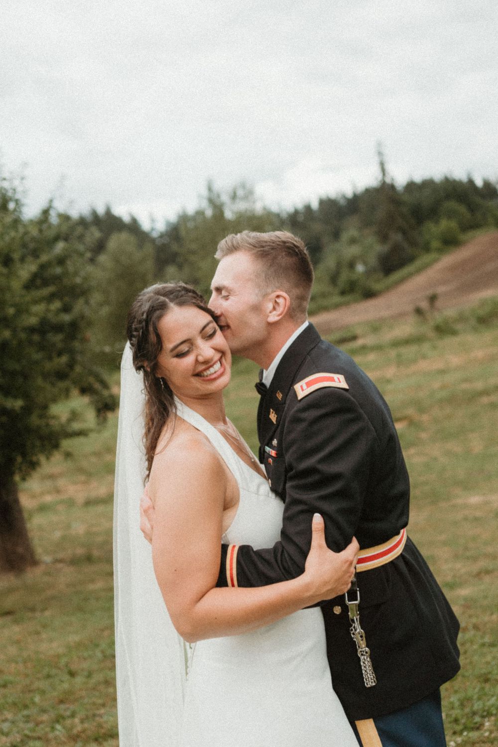 Military groom kisses bride tenderly during outdoor wedding photoshoot.
