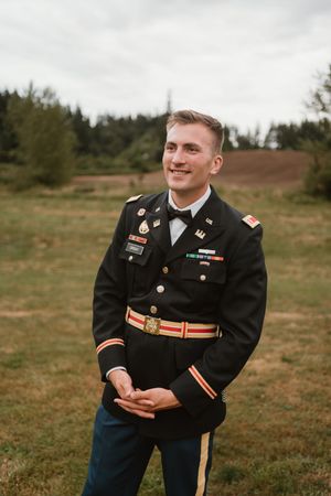 Military officer in formal dress uniform smiling outdoors during wedding.
