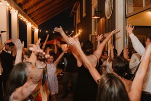 Wedding guests dancing and celebrating with raised arms under venue lighting.