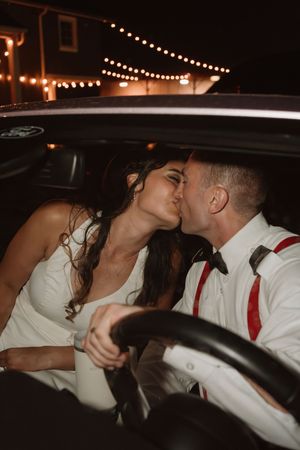 Romantic moment between newlyweds in their getaway car under string lights.