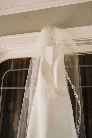 White wedding dress and veil hanging by window with natural light streaming in.