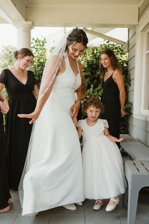 Wedding party helps with dress arrangements on an outdoor porch.