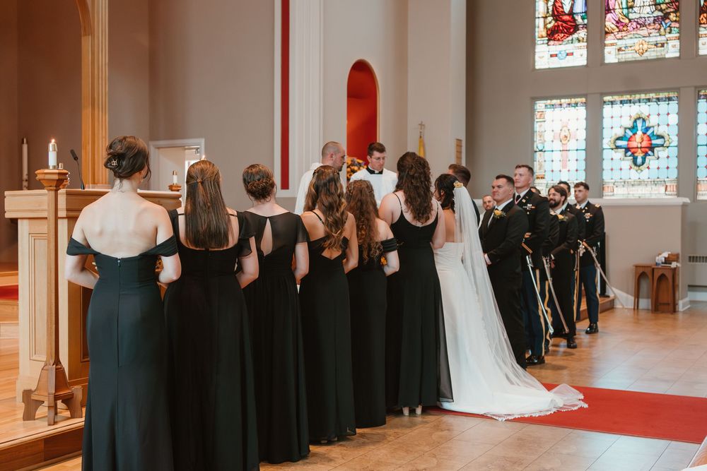 Wide shot of church wedding ceremony with bridesmaids in black dresses lining the aisle.