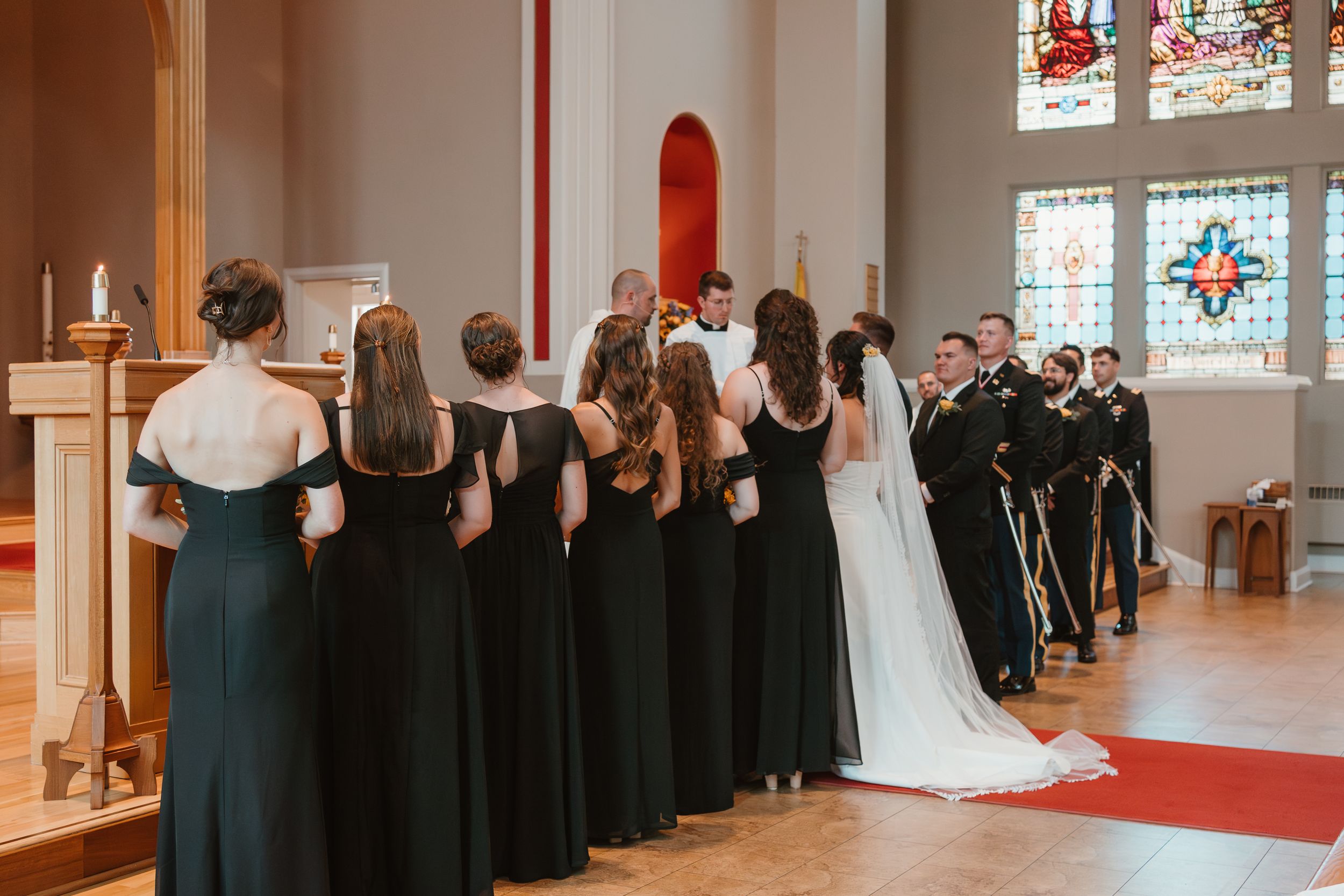 Wide shot of church wedding ceremony with bridesmaids in black dresses lining the aisle.