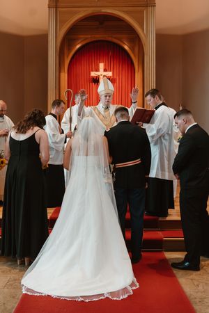 Wedding ceremony in a church with white decor and red altar backdrop.