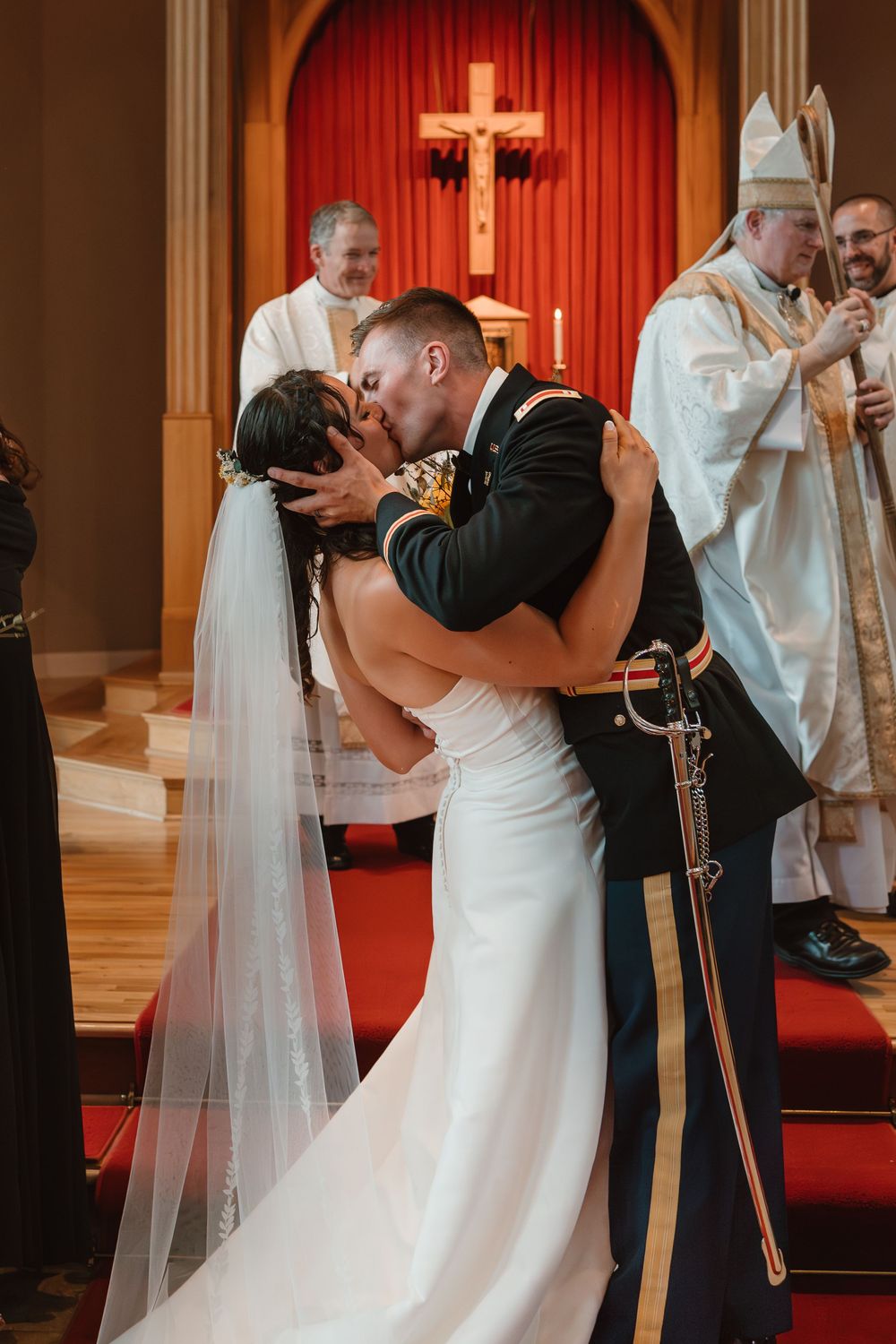 First kiss at wedding ceremony with bride in white dress and groom in military uniform.
