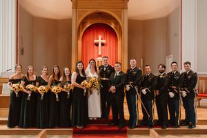 Wedding party in black attire standing in church with cross illuminated in background.