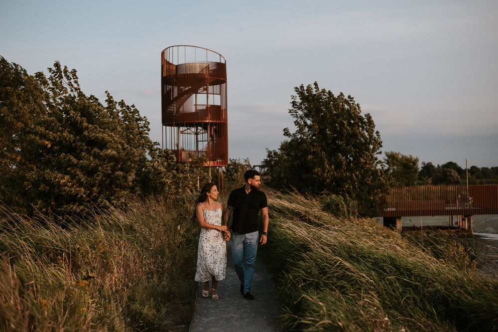 Photo de couple en extérieur, deux personnes marchant dans les herbes hautes près d’une structure rustique