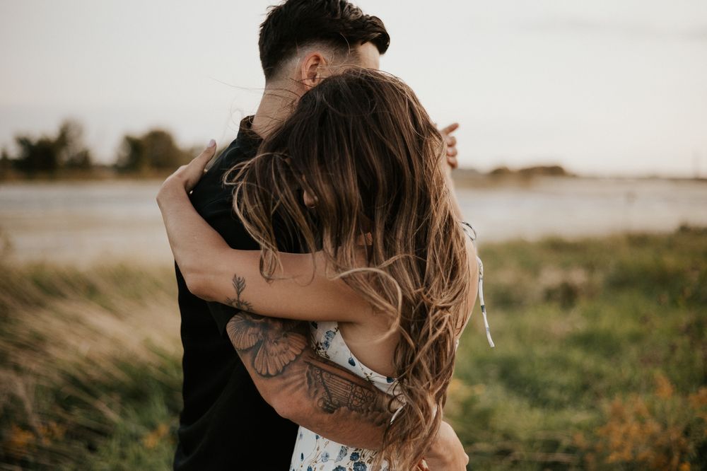 Portrait couple en extérieur, deux personnes enlacées près de l’eau et des herbes hautes