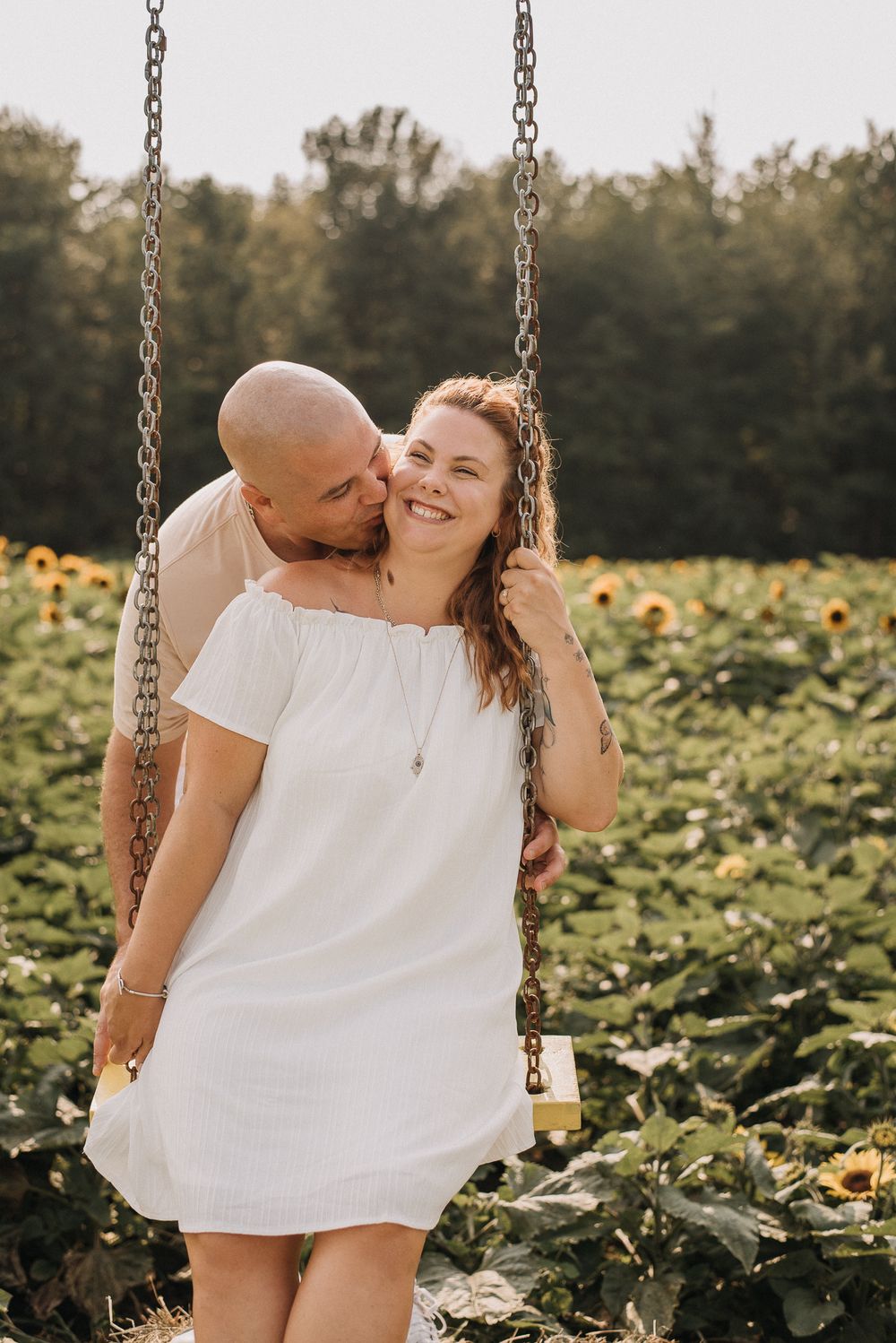 Séance couple lifestyle dans un champ de tournesols, robe blanche et balançoire