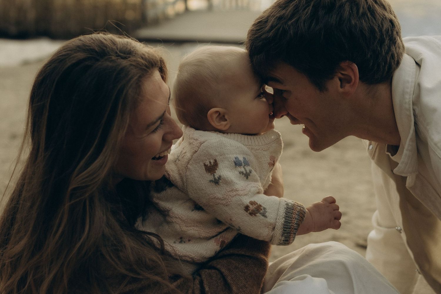 mom holding a baby while dad is touching the baby's face with his nose while they're all being captured by family photographer in Stockholm