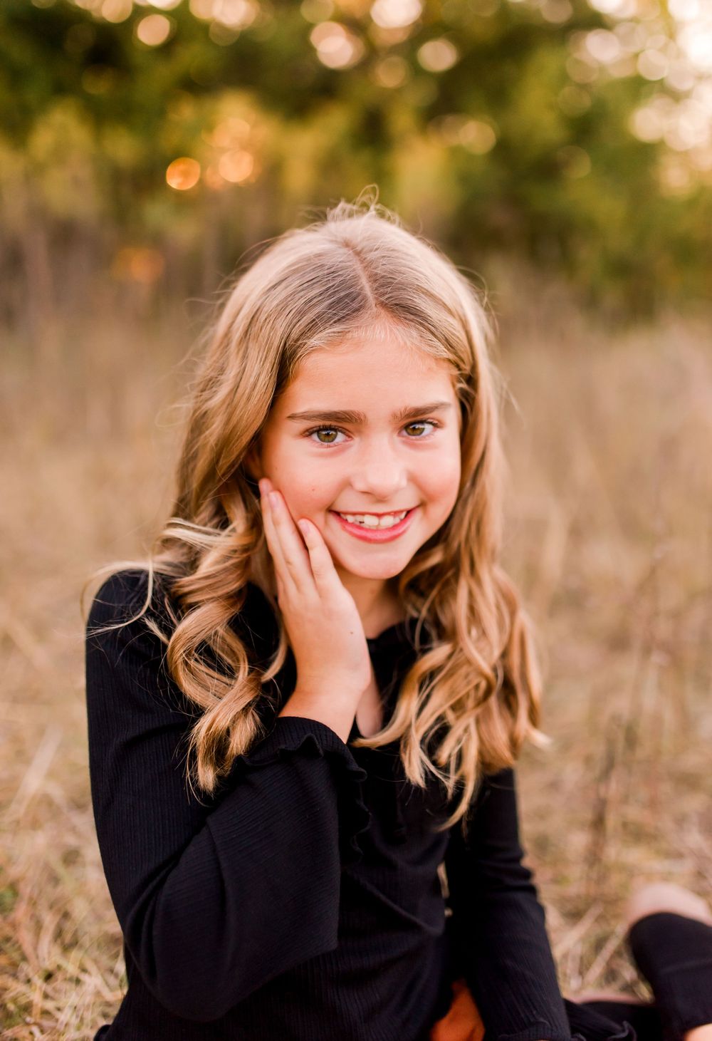 Young person in a black sweater sitting outdoors with wavy blonde hair and natural lighting during golden hour.