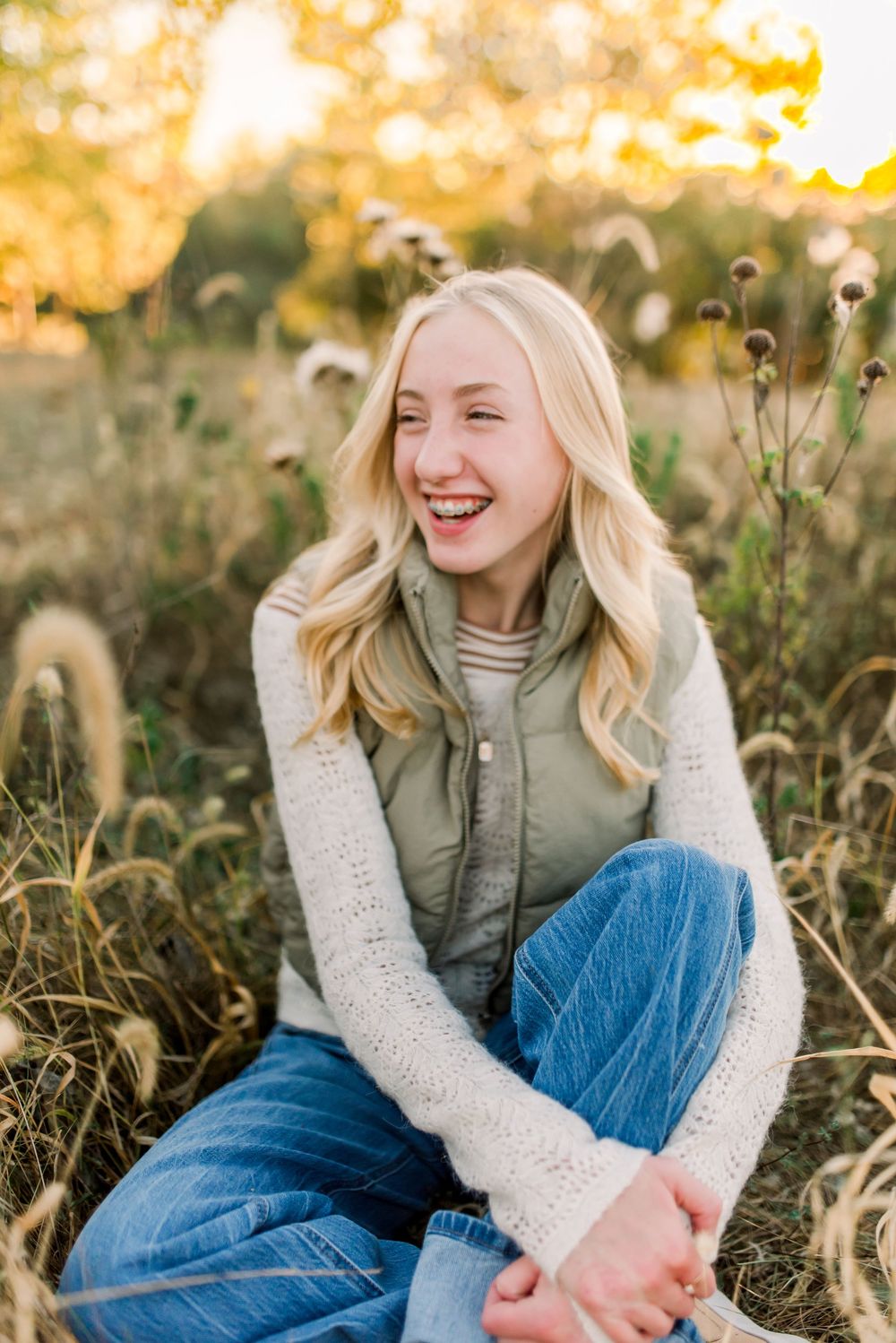 A person in a green vest and white sweater sits in a wildflower field during golden hour.