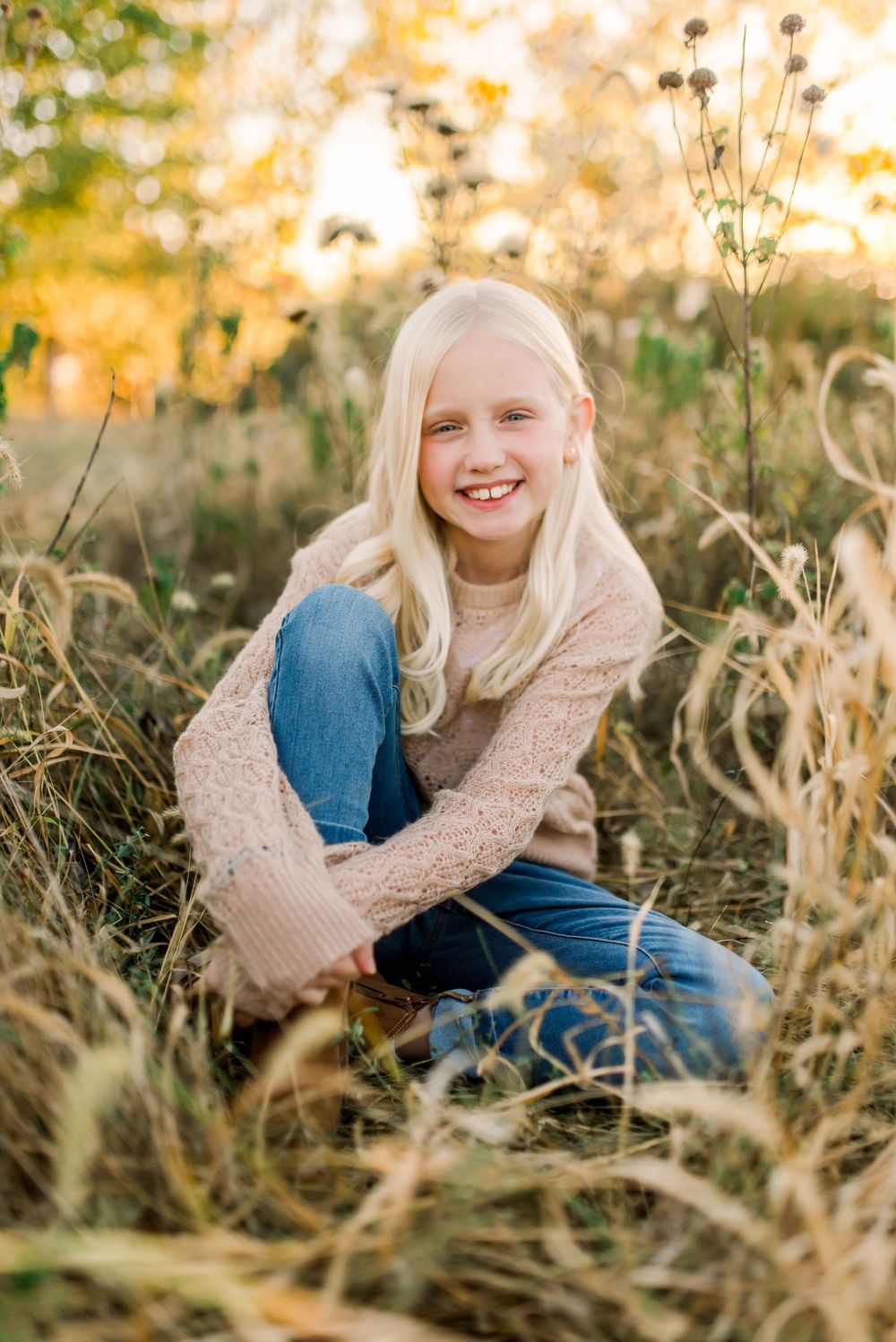 Joyful portrait in a golden autumn field with tall grass and warm sunset lighting wearing a beige sweater and jeans.