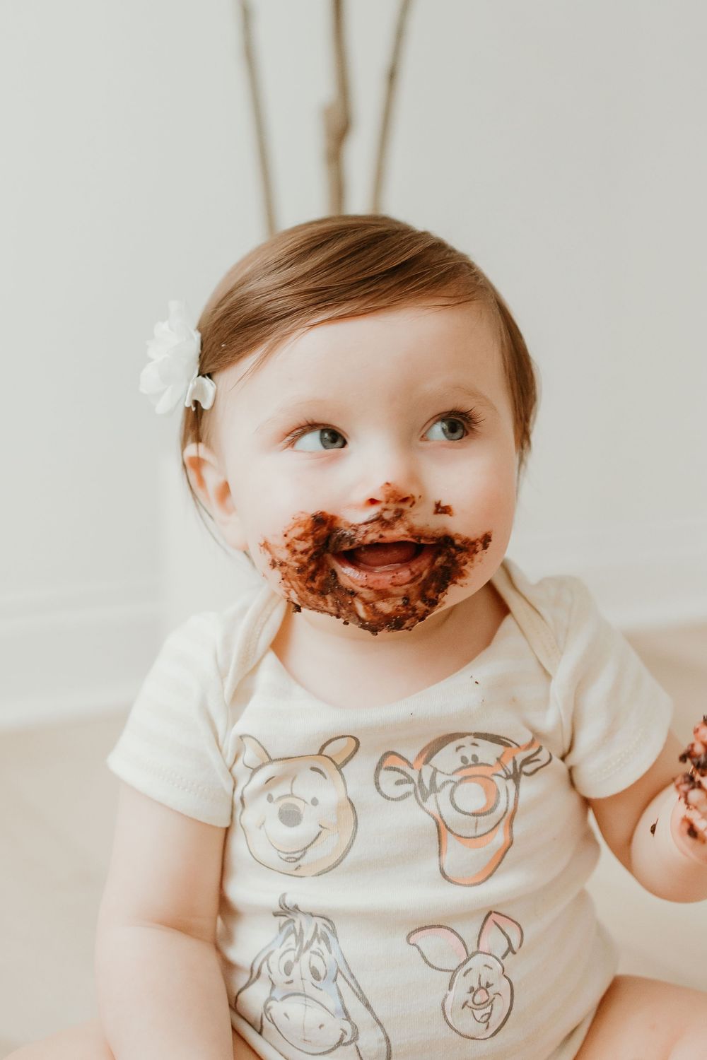 Baby wearing a white animal print onesie with chocolate smeared around their mouth.