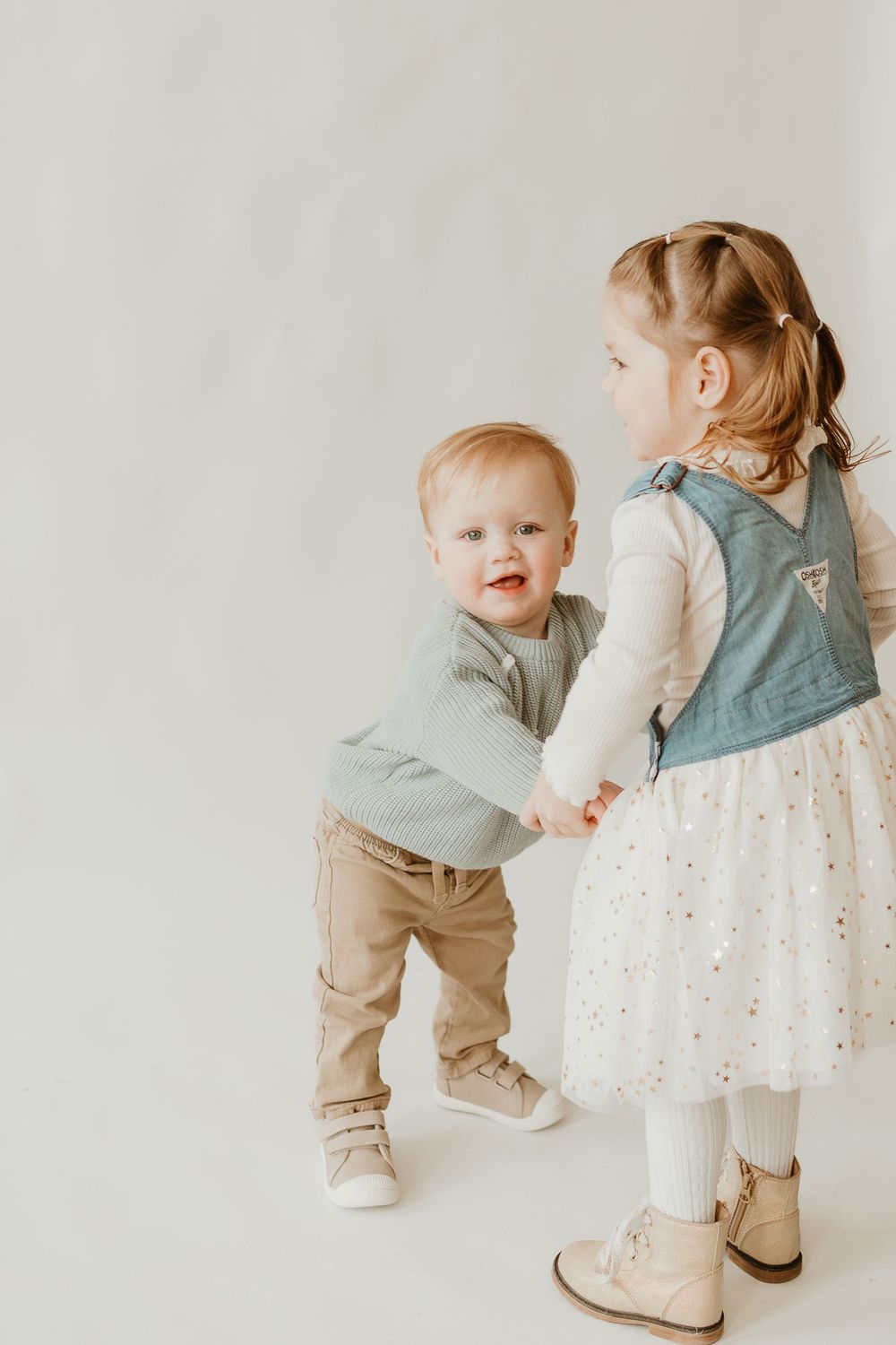 Two young children in soft neutral tones interact sweetly together against a light background in a series of candid moments.