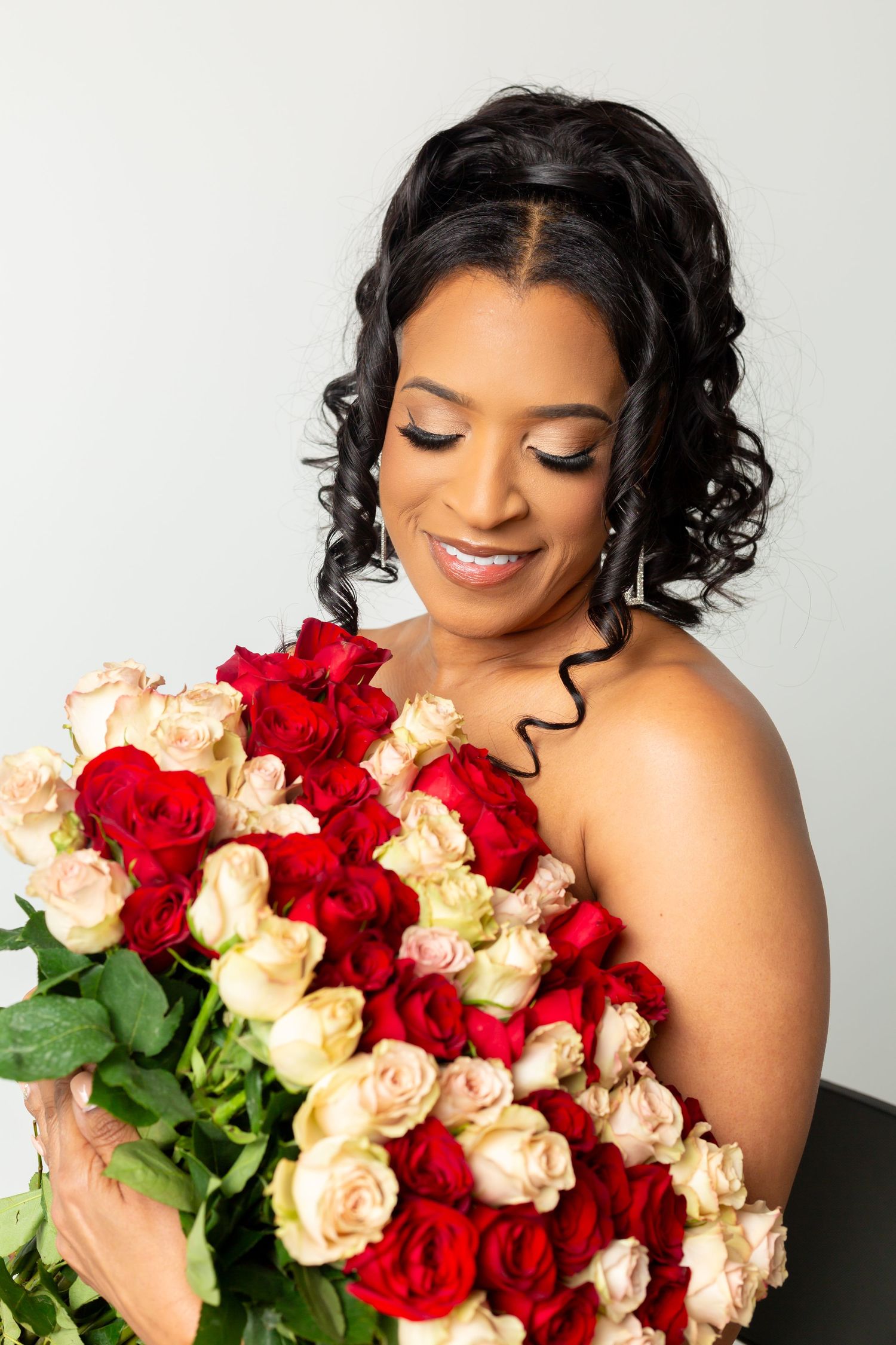 A joyful person smiling while holding a stunning bouquet of red and cream colored roses against a white background.