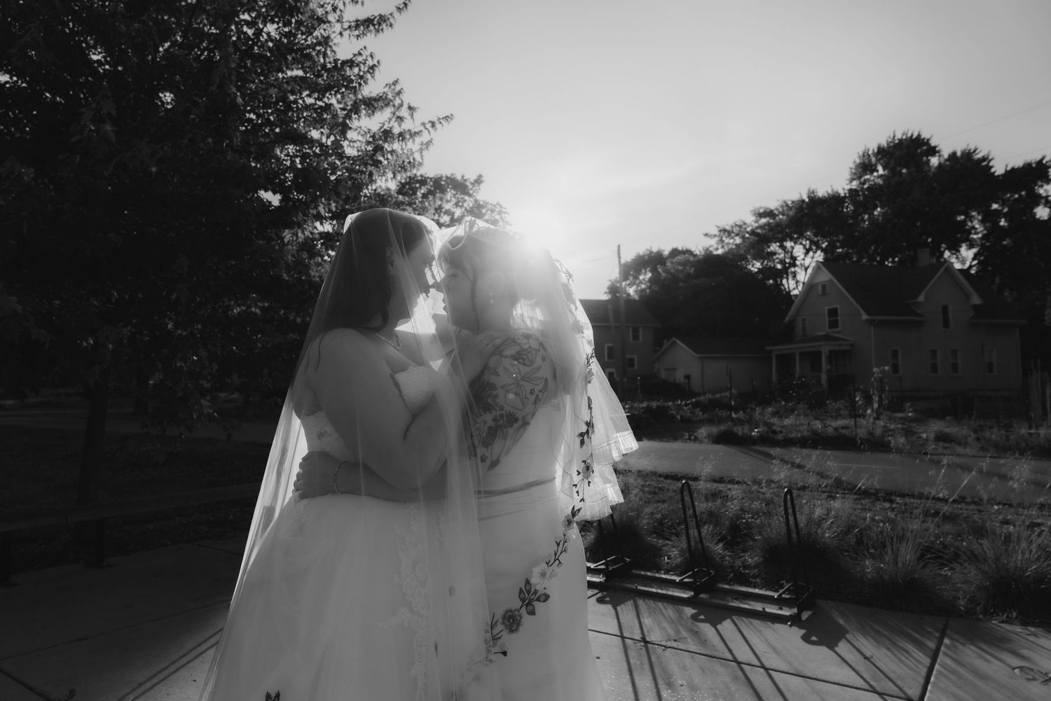 Two brides sharing joyful moment while holding colorful bouquets on sunny wedding day.