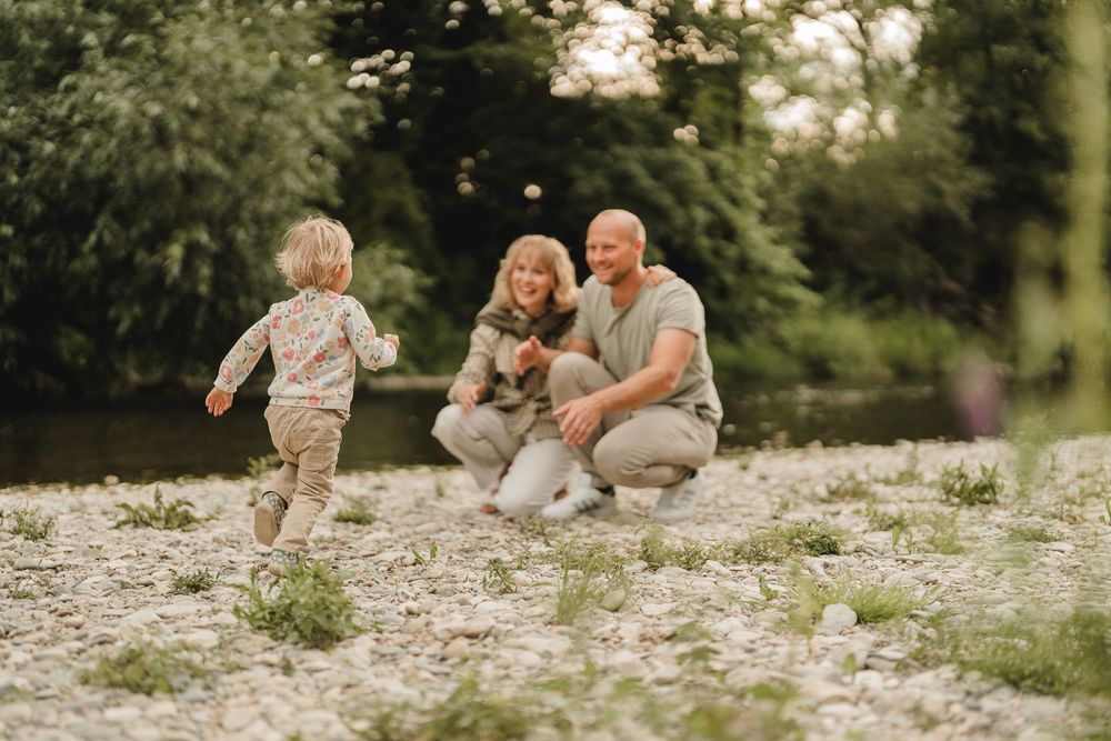 Liebevolle Eltern spielen mit Kleinkind am Wasser bei einem Fotoshooting in Munderkingen. Fotografiert von Ramona Maier