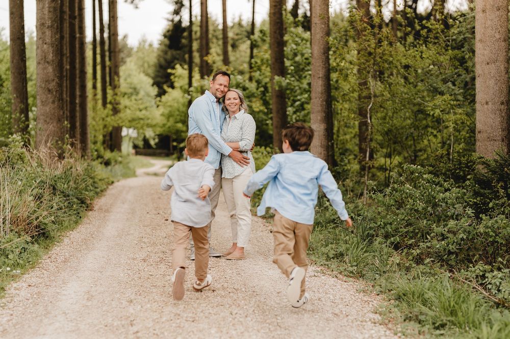 Familie spaziert und spielt gemeinsam auf einem Waldweg an einem sonnigen Tag.