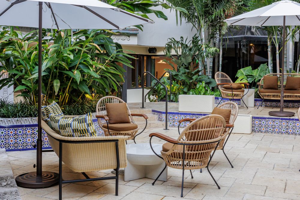 Luxurious outdoor lounge area with rattan chairs, umbrellas and tropical plants surrounding a tiled patio.