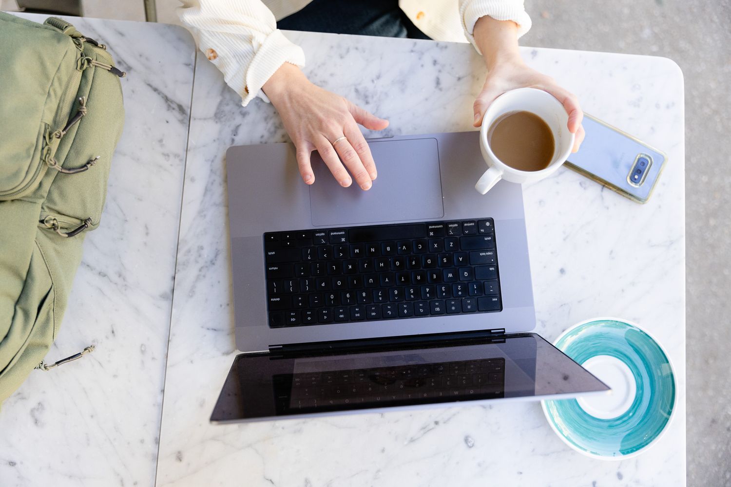 Overhead workspace scene with laptop, keyboard and coffee on marble surface.