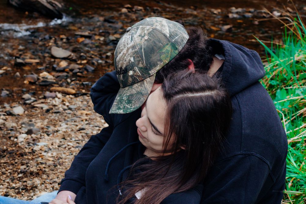 A couple sharing a tender moment on forest ground with fallen leaves.