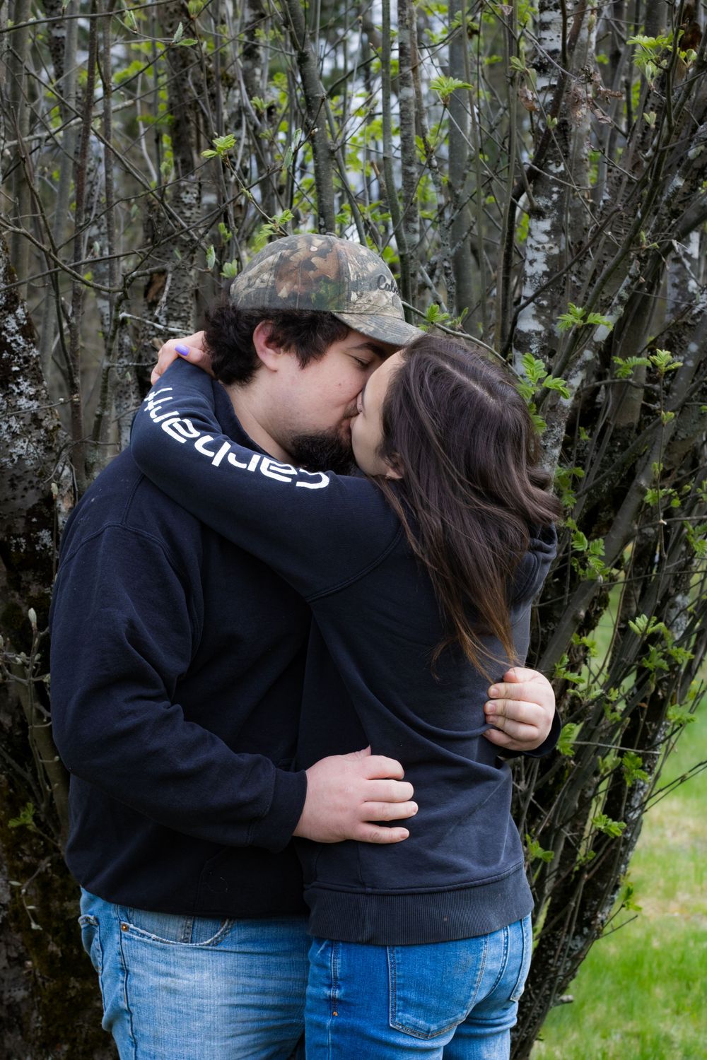 A couple sharing a romantic kiss against a backdrop of spring trees and bushes.