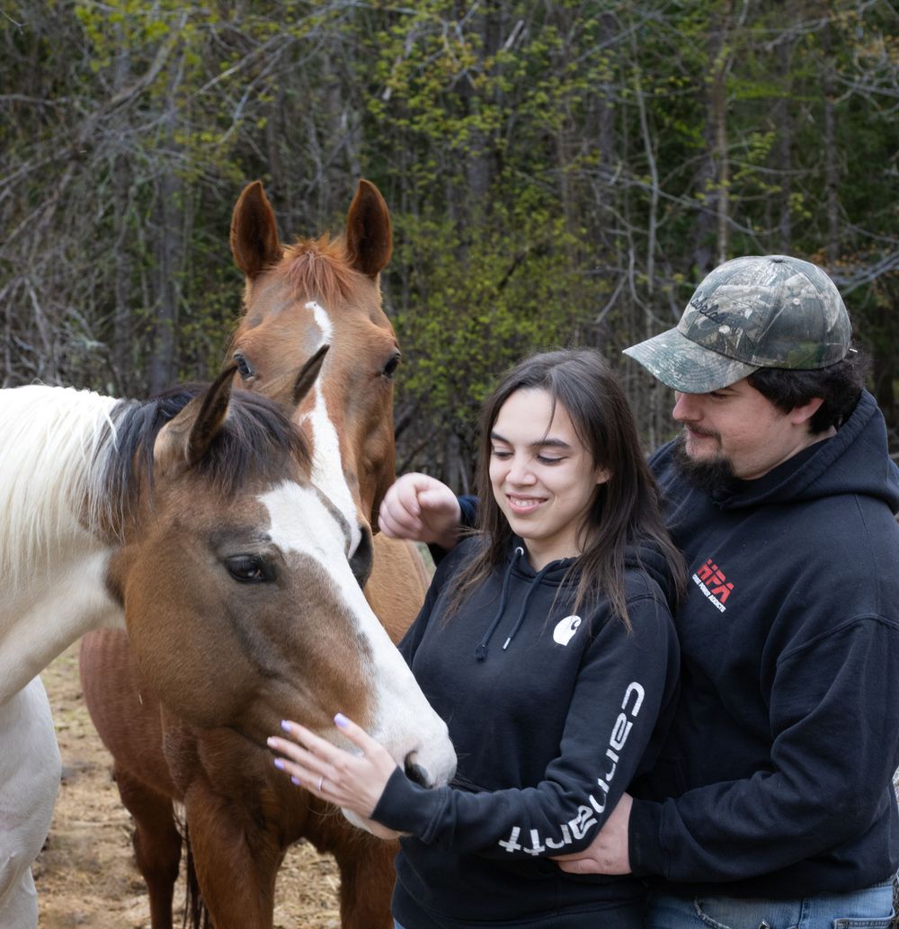 A couple petting a brown and white horse while sharing a sweet moment outdoors.