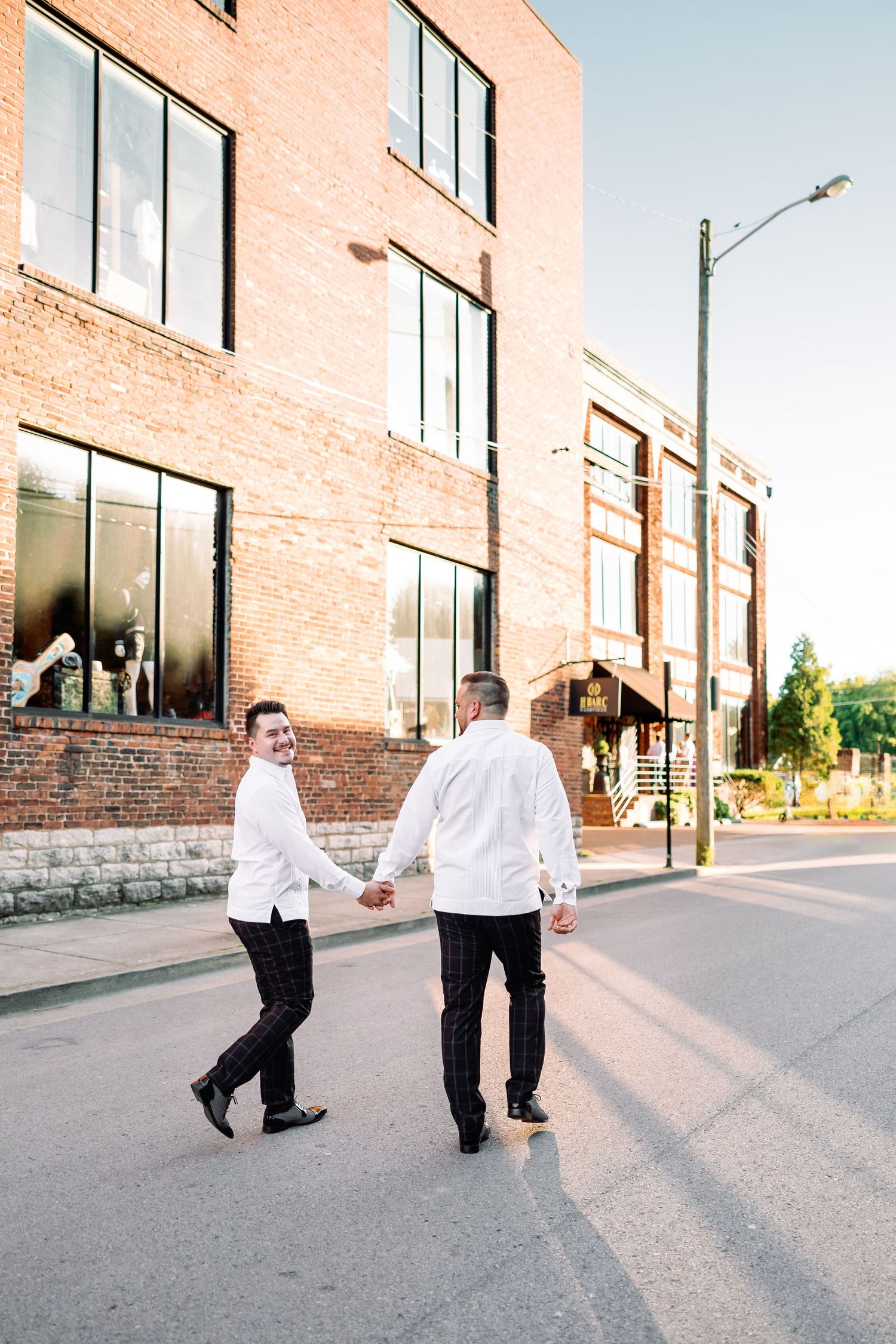 Playful LGBTQ grooms walking and posing outside a brick building in formal attire in Nashville, TN.