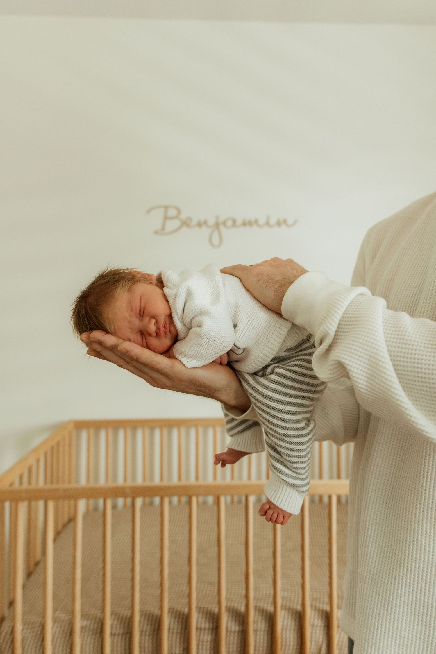 Newborn baby lying on caregiver's lap in warm natural lighting.
