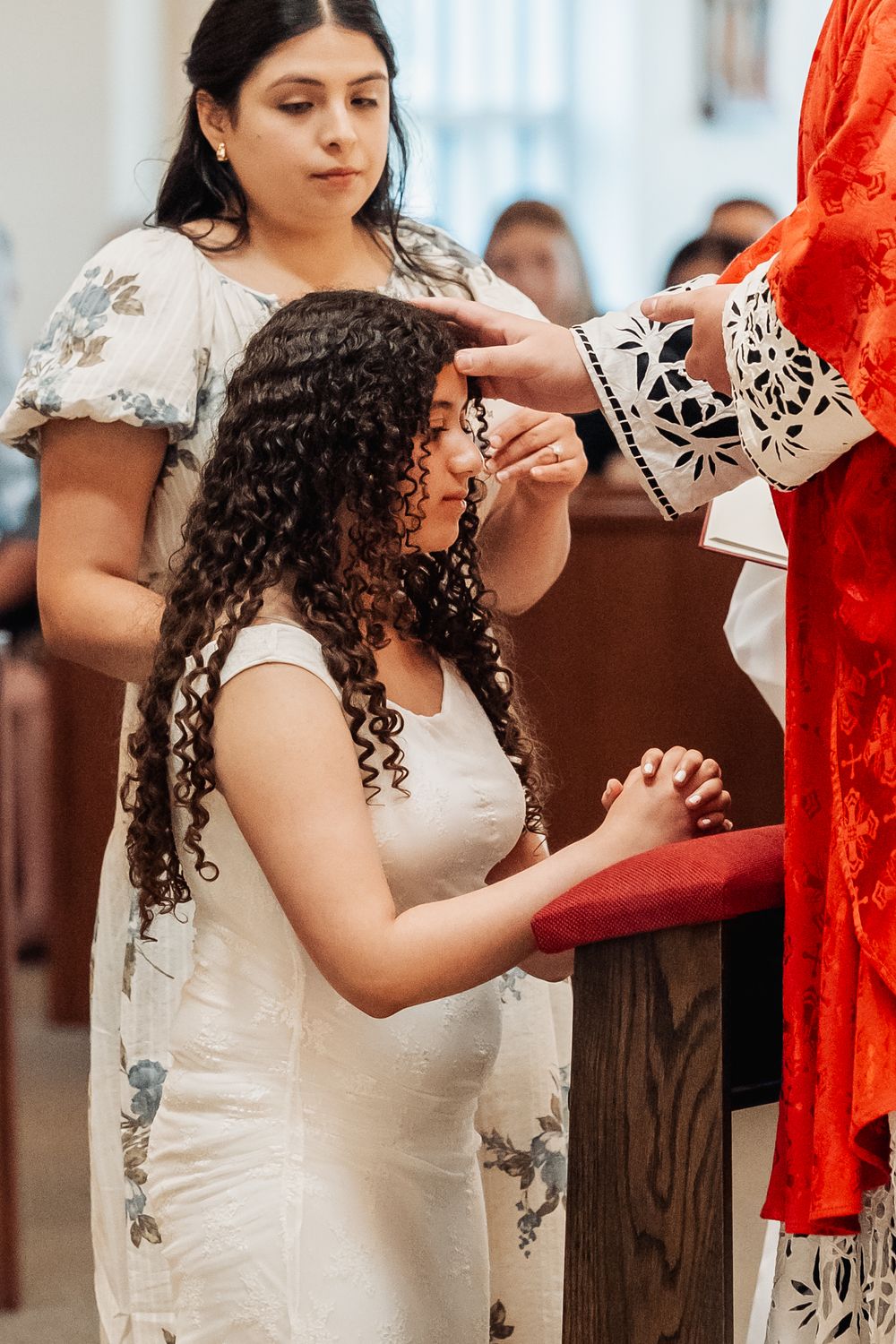 Young girl in white dress receives communion at church altar during a religious ceremony.