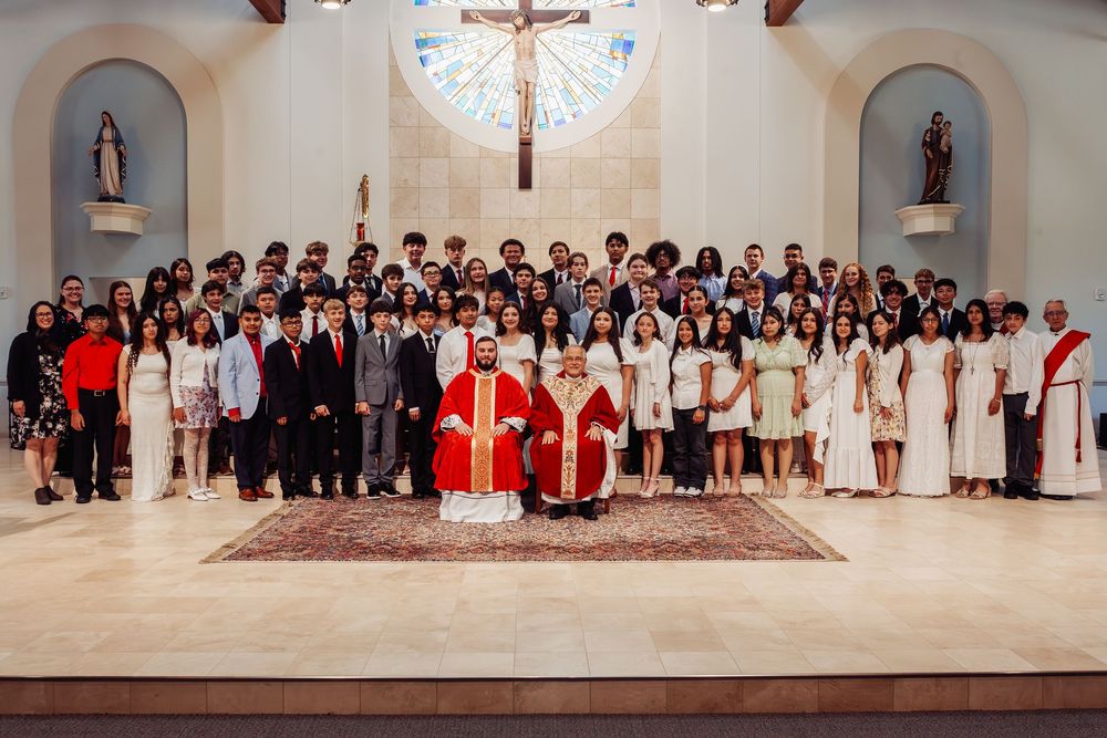 Catholic Confirmation ceremony group photo with priest in red vestments and confirmands in white robes inside a church.
