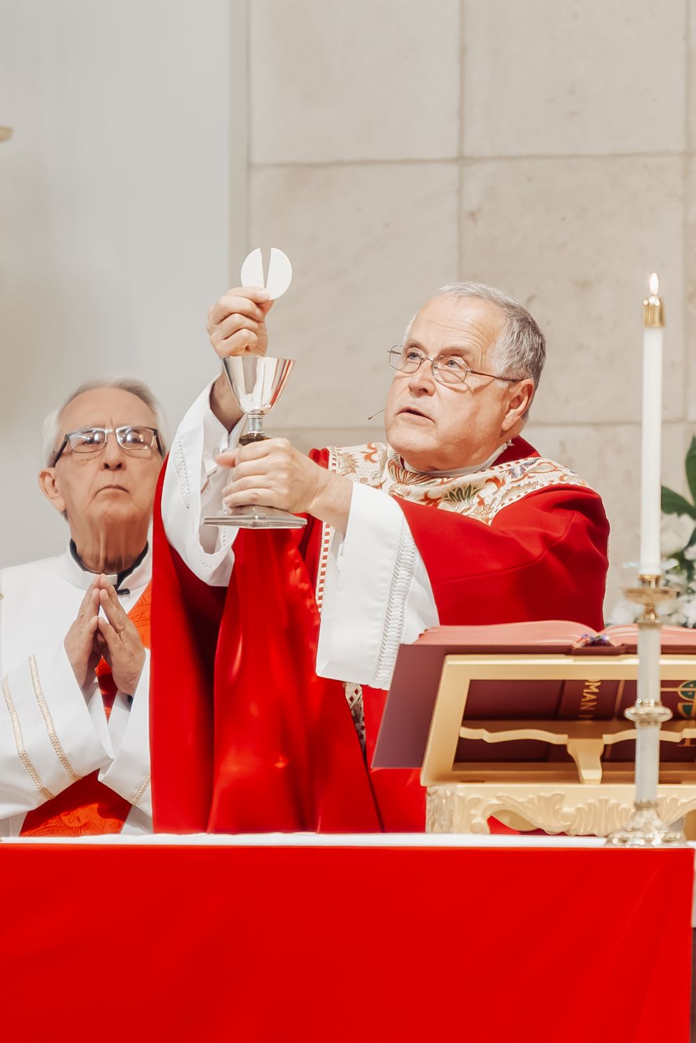 Catholic priest in red vestments elevates the chalice during Holy Mass at the altar.