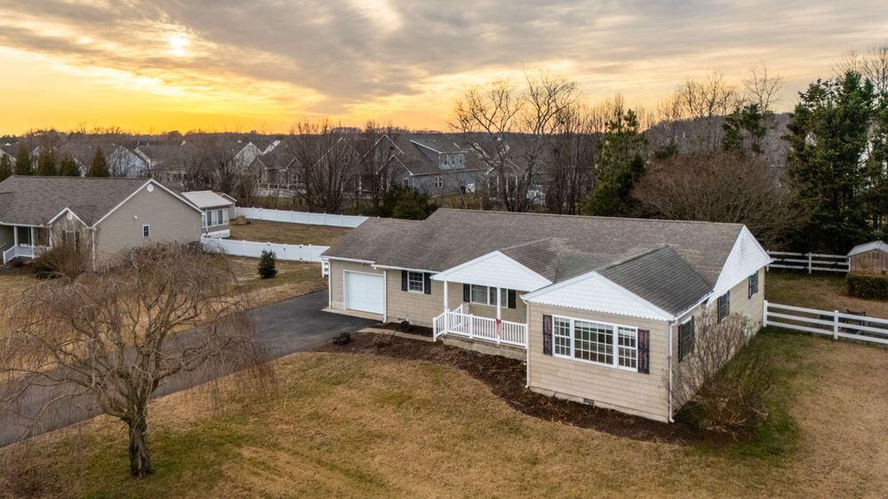 Aerial view of a white ranch home with white trim during sunset with golden clouds in the sky.
