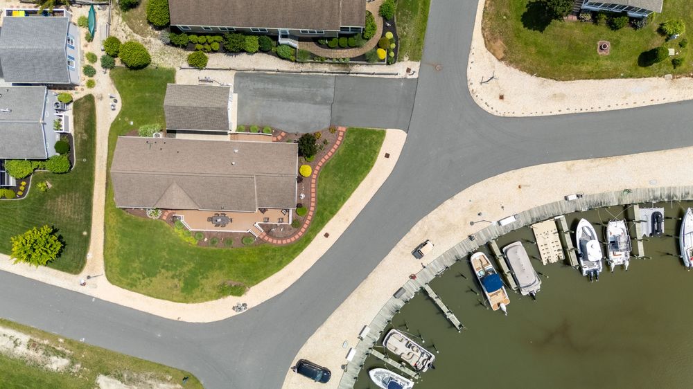 Aerial view of Delaware waterfront homes with boat docks and moored vessels along a curved residential street.