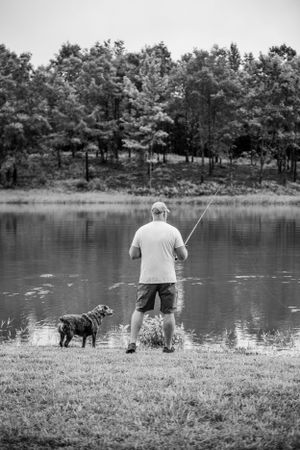 Person and dog enjoying a peaceful afternoon by a serene lake in black and white.