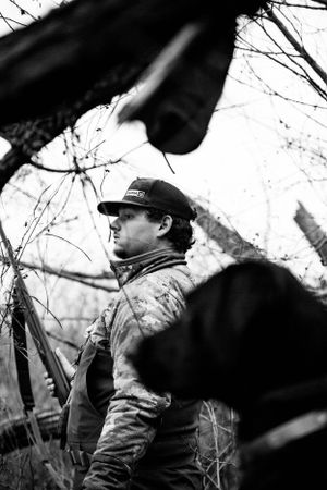 Duck hunter in winter camouflage moving through brush with hunting gear.