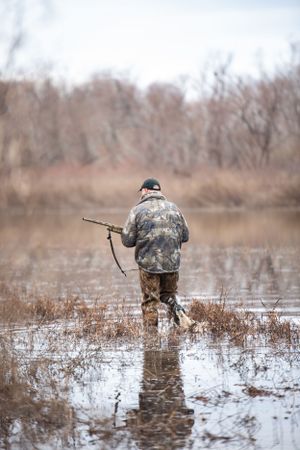 Hunter wearing camouflage navigating through shallow flooded wetlands during waterfowl season.