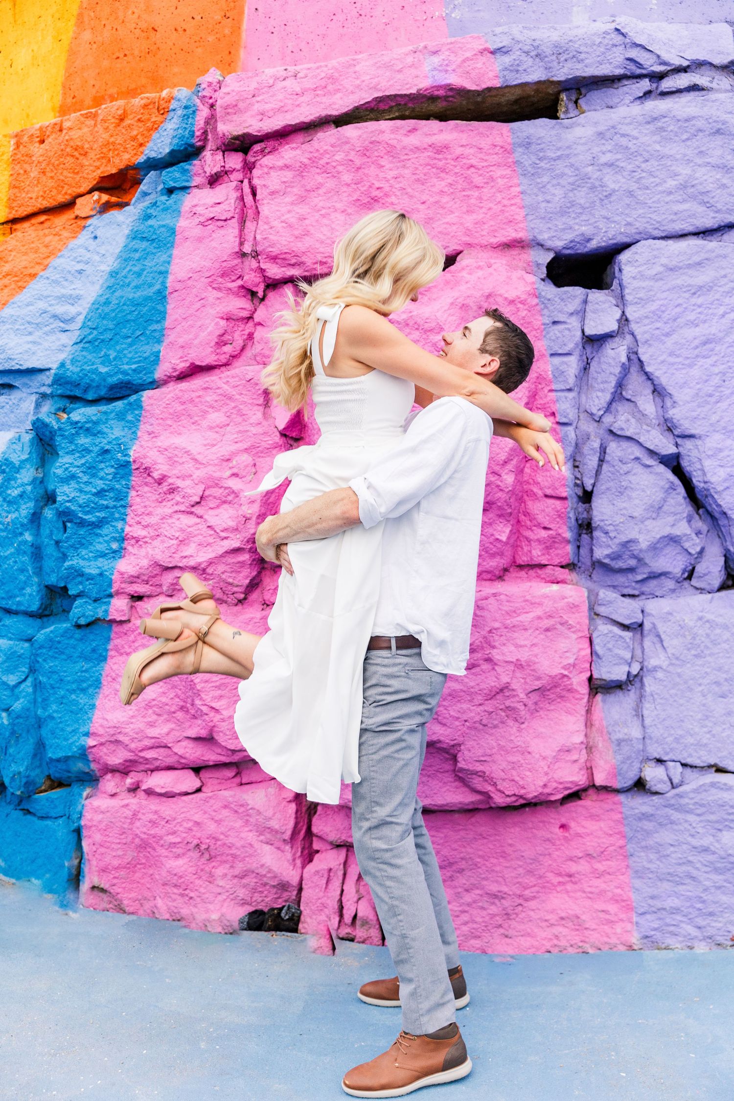 A romantic lift pose against a colorful rainbow painted rock wall background.